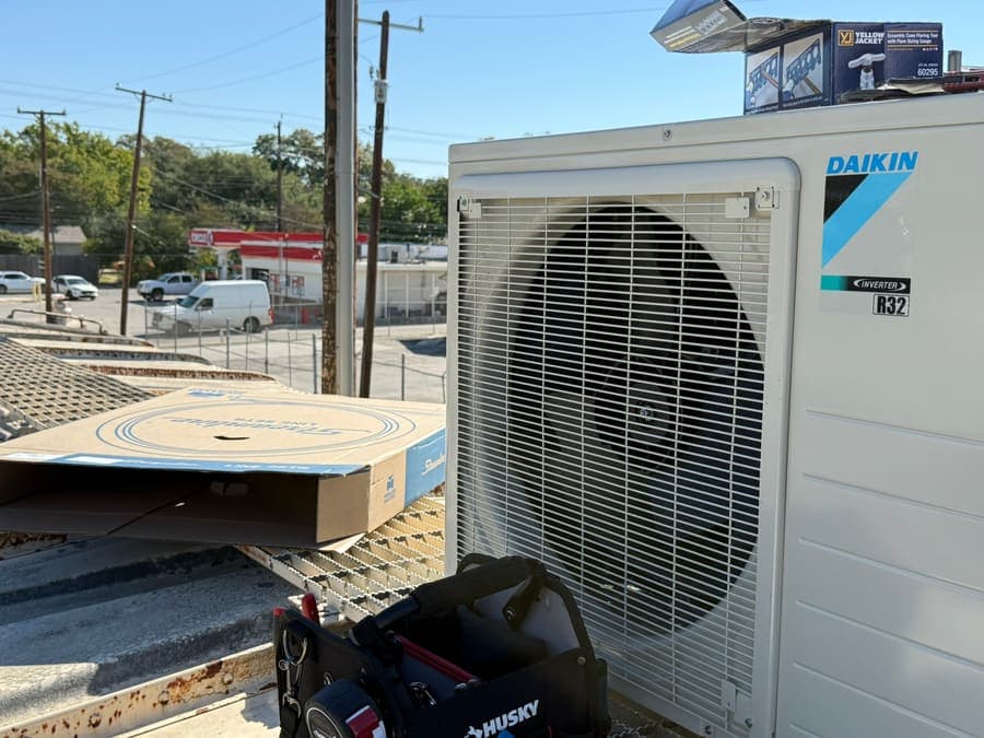 A Daikin inverter outdoor unit and a tool bag on a metal work deck